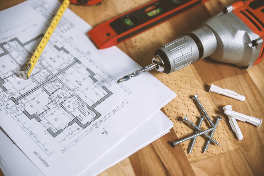 Floor plans, spirit level and drill on a workbench